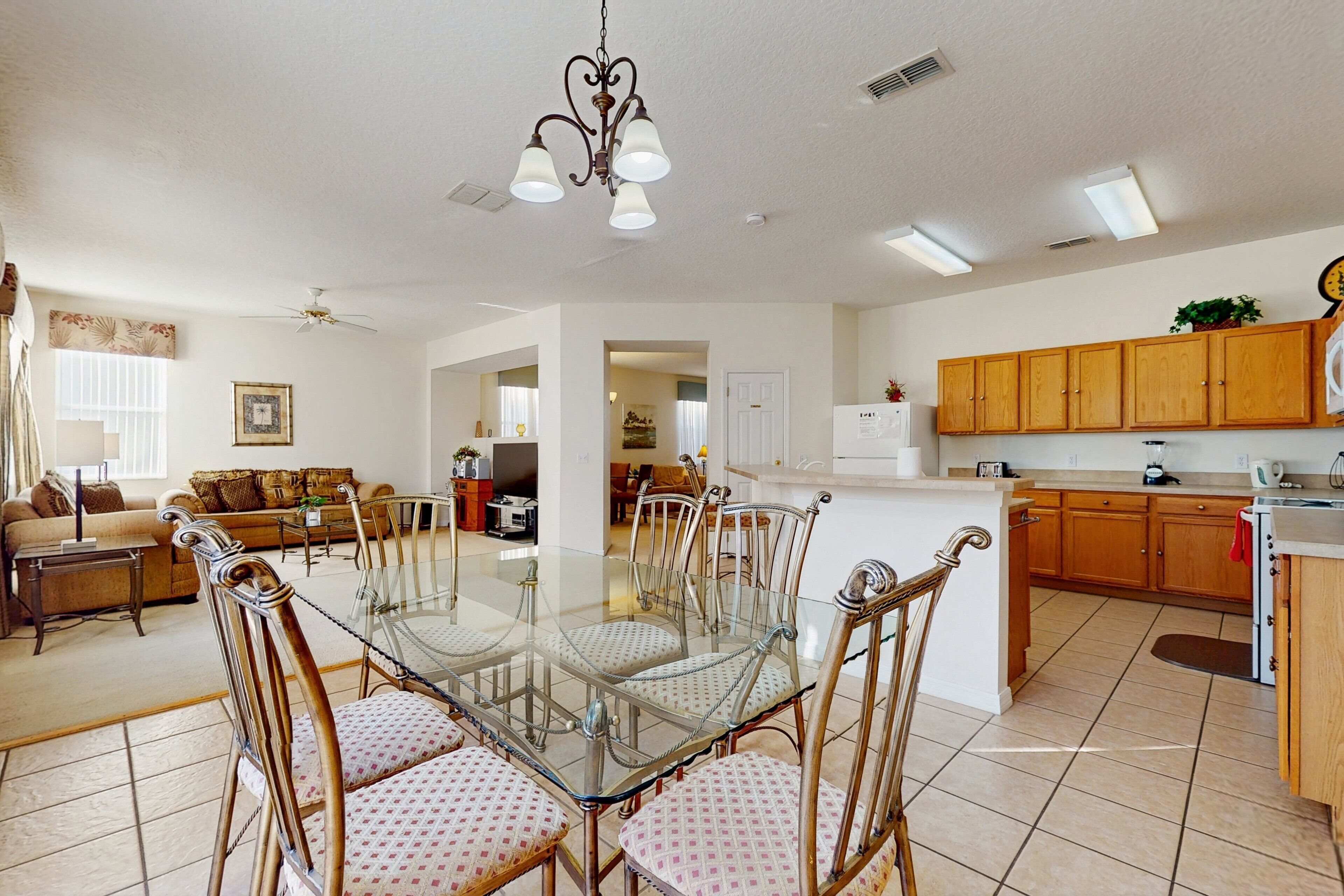 A spacious living area with a glass dining table, chairs, and a ceiling fan.