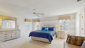 Quarto com cama, cômoda, mesas de cabeceira e ventilador de teto.