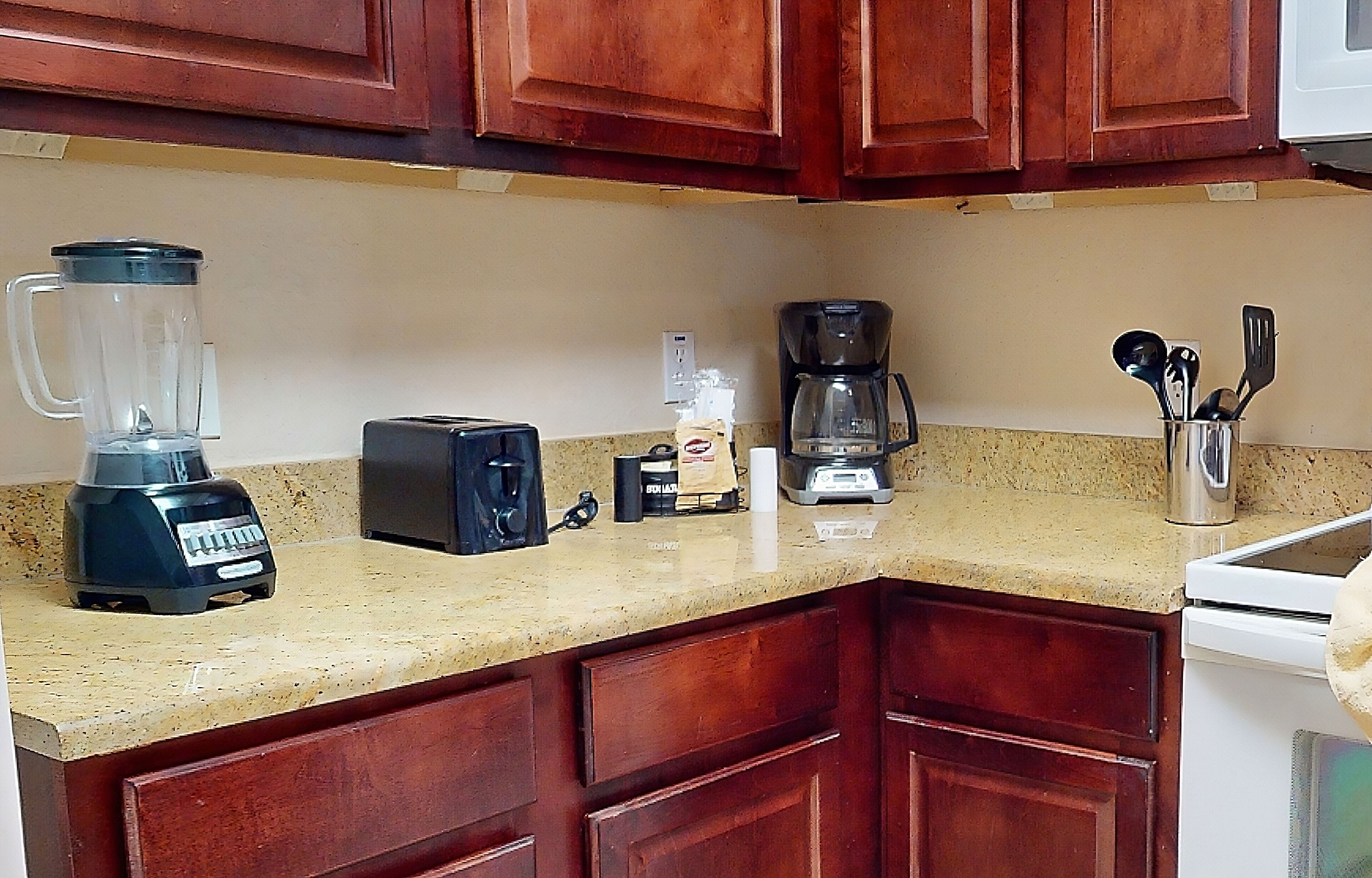 A kitchen with wooden cabinets, a blender, a toaster, a coffee maker, and a utensil holder.