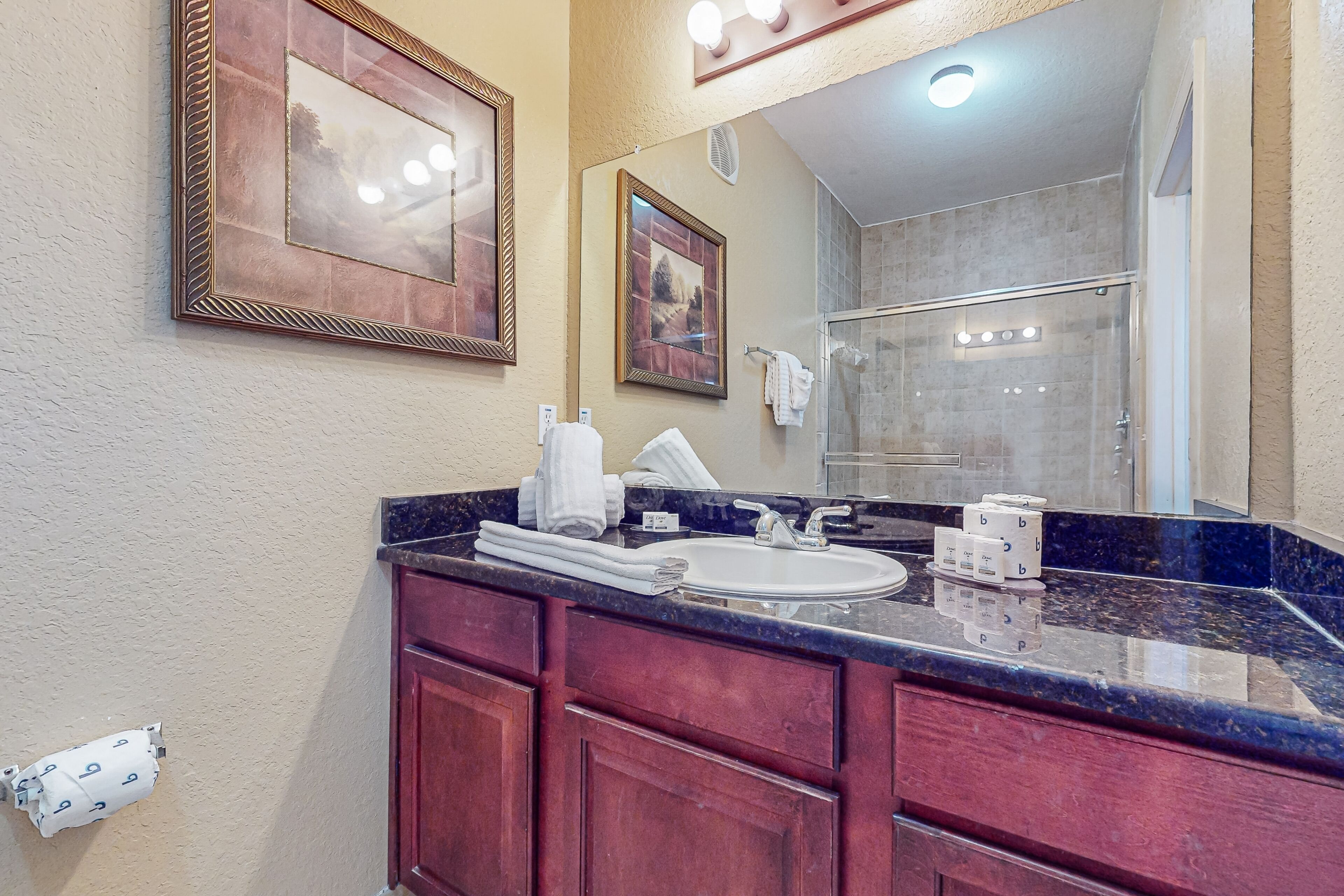A bathroom with a marble countertop, a sink, a mirror, and a shower area.