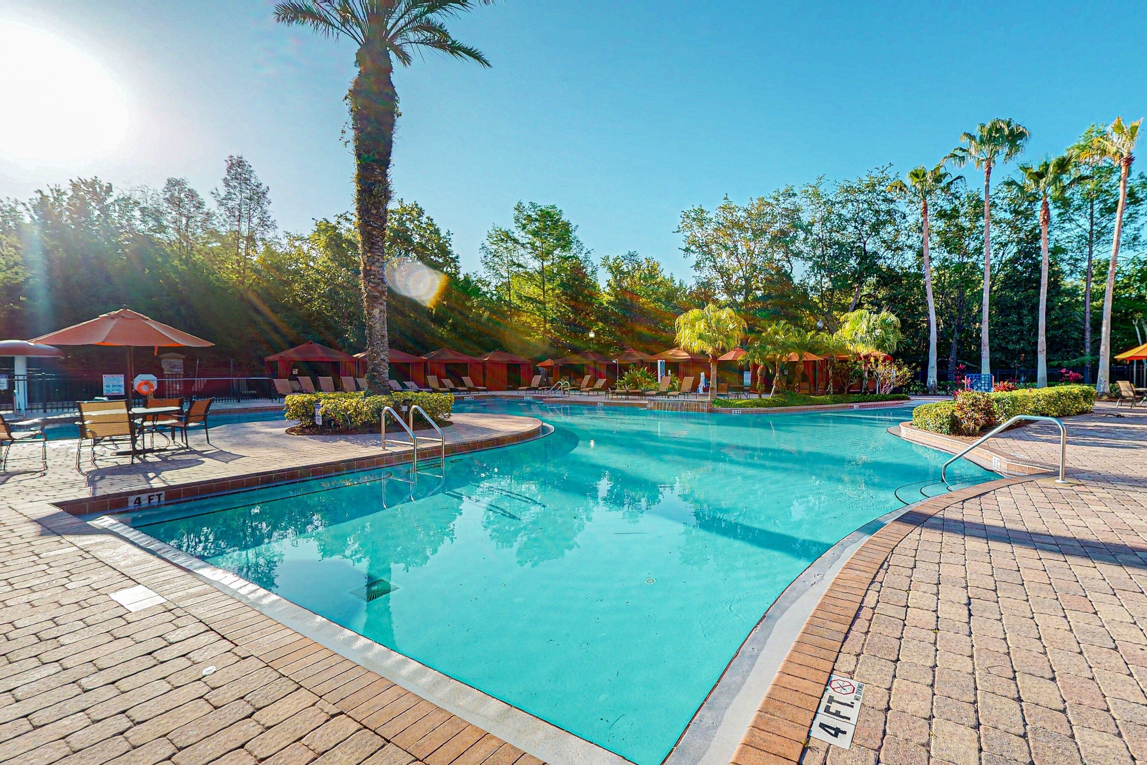 A swimming pool with a 4 FT depth marker, surrounded by lounge chairs and palm trees.