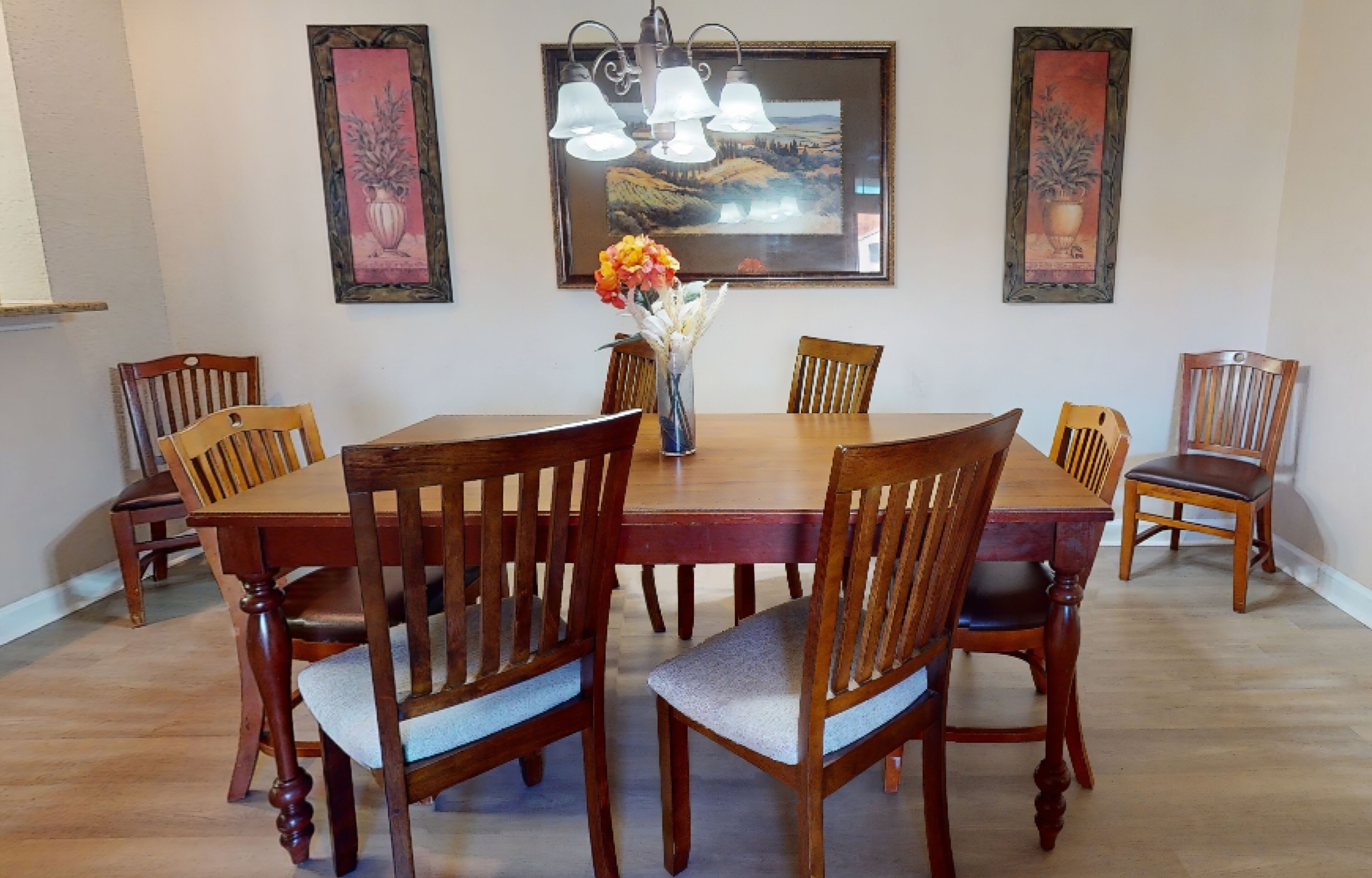 A dining room with a wooden table and chairs, a vase with flowers, and framed artwork on the wall.