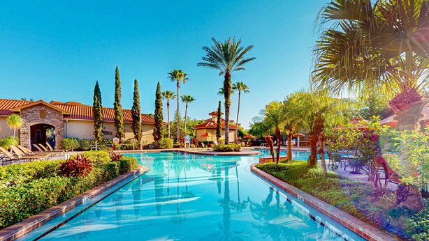 A swimming pool with a tiled deck, surrounded by palm trees and a building with a red-tiled roof. - Resort Condo Close to Theme Parks With On-site Pool, Bar, Restaurant, & gym (Davenport)