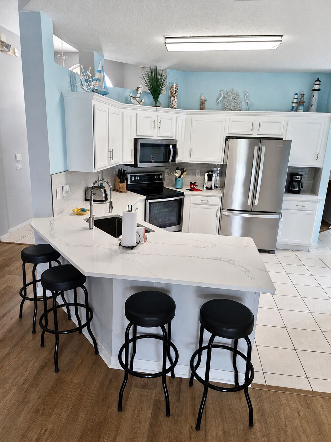 A modern kitchen with white cabinets, stainless steel appliances, a central island with stools, and decorative nautical items.