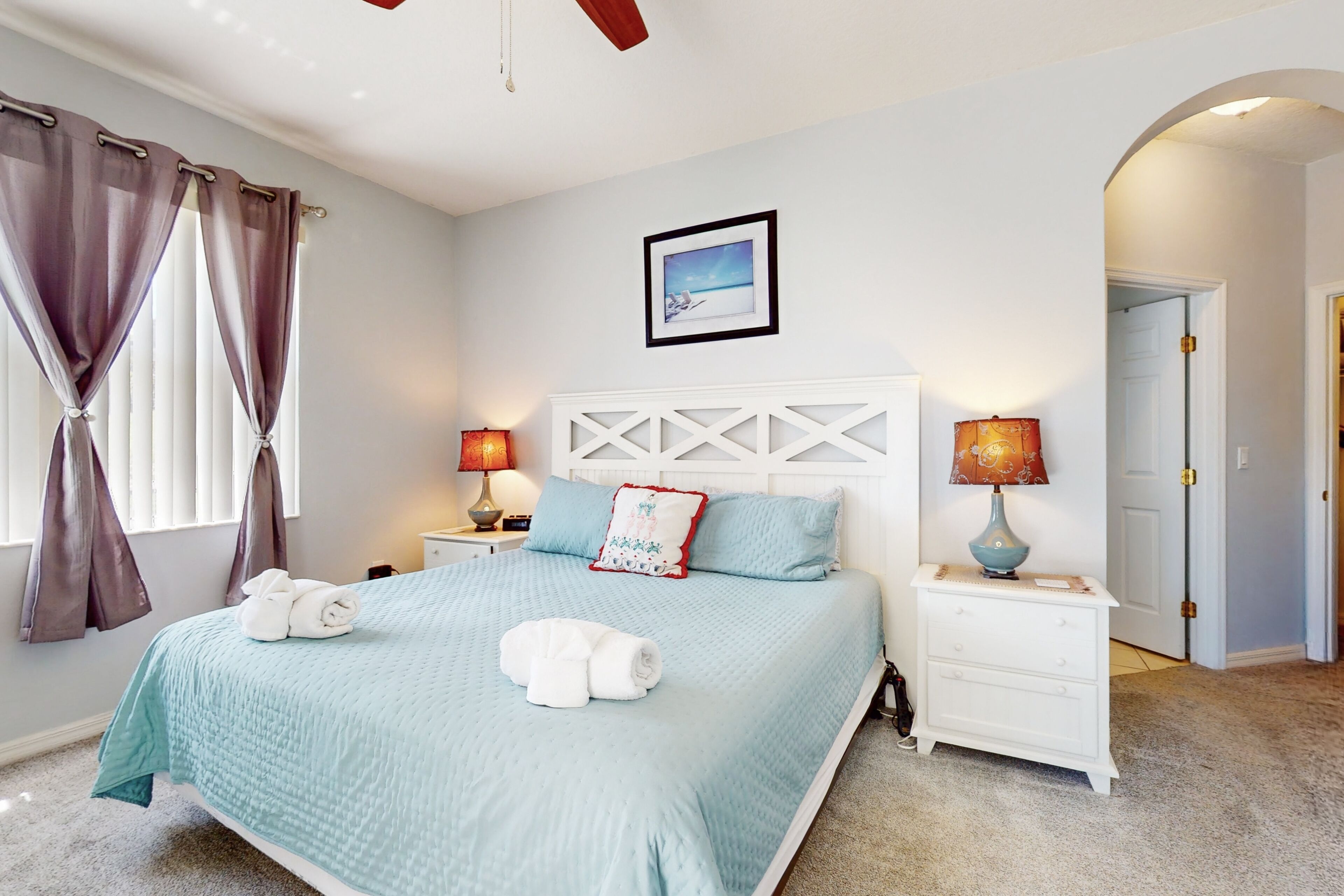 A bedroom with a bed, two nightstands, a white dresser, a ceiling fan, and a door.