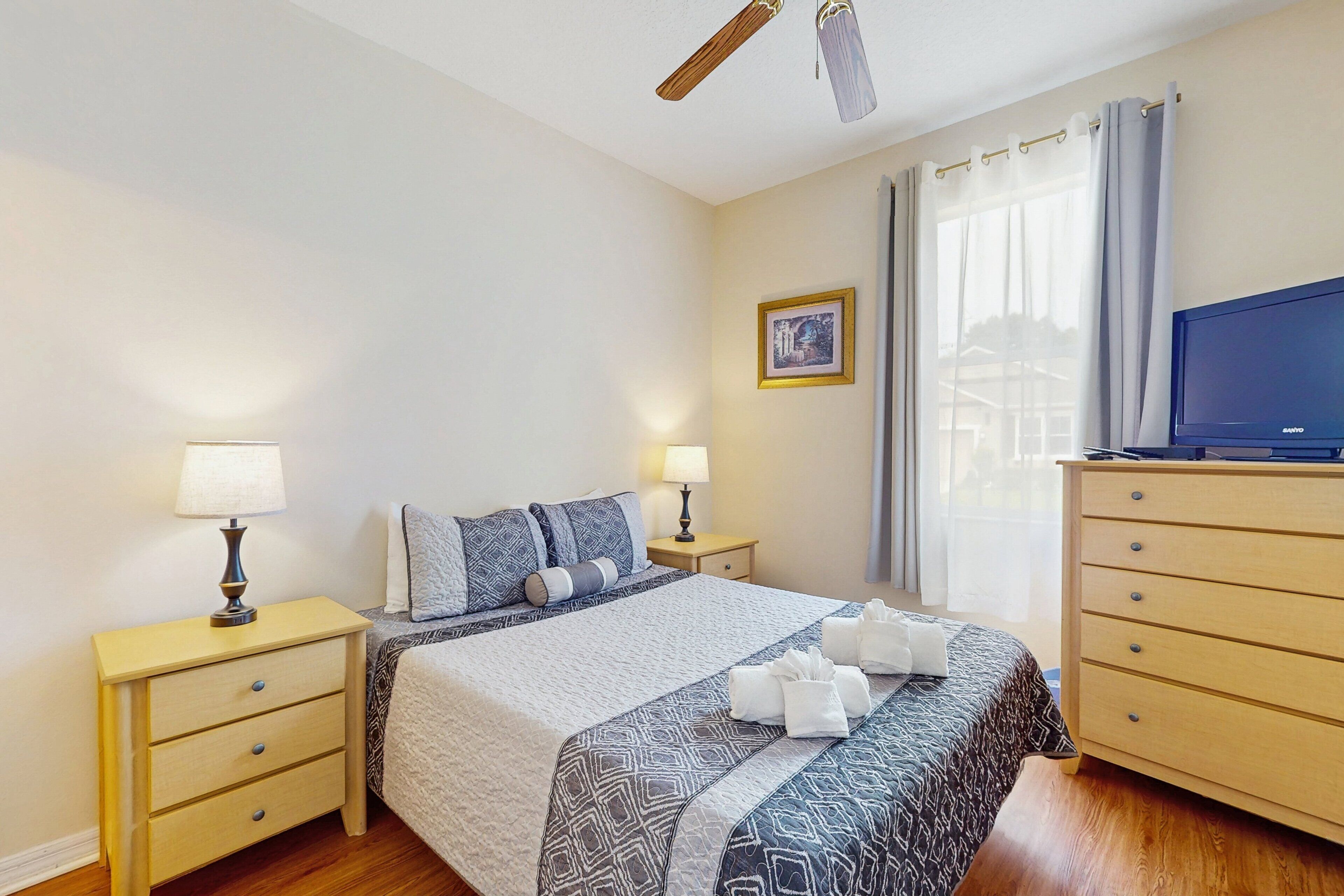 A hotel room with a bed, two bedside tables with lamps, a television, and a window with curtains.