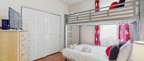 A bunk bed room with a wooden dresser, a ceiling fan, and a window with curtains.