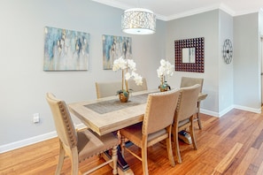 Un coin repas avec une table en bois, quatre chaises, un vase de fleurs et deux tableaux abstraits accrochés au mur.