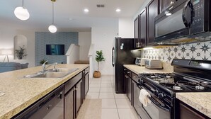 A modern kitchen with granite countertops, stainless steel appliances, and dark wooden cabinets. - Solterra Escape Private Pool Café, Tennis & Water Park With Lazy River (Davenport)