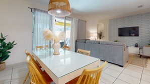 A modern living room with a glass dining table, wooden chairs, a grey sofa, a TV mounted on a brick wall, and a large woven pendant light. - Solterra Escape Private Pool Café, Tennis & Water Park With Lazy River (Davenport)