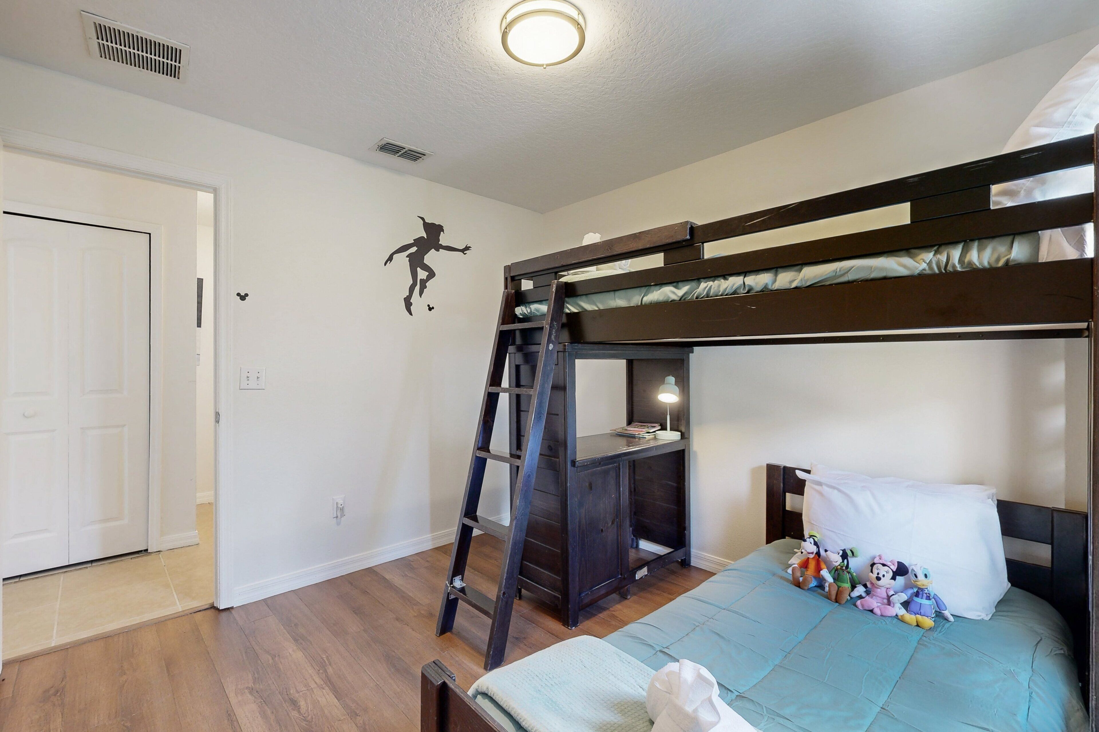 A bunk bed with a ladder, a desk with a lamp, and toys on the bed.
