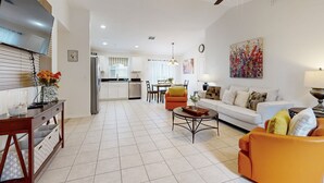 A spacious living room with a sofa, coffee table, and a TV mounted on the wall. There is a kitchen area in the background with a dining table and chairs. - Dog-friendly, Private Pool , Central AC, Full Kitchen, Wifi, Snow-bird Friendly (Davenport)