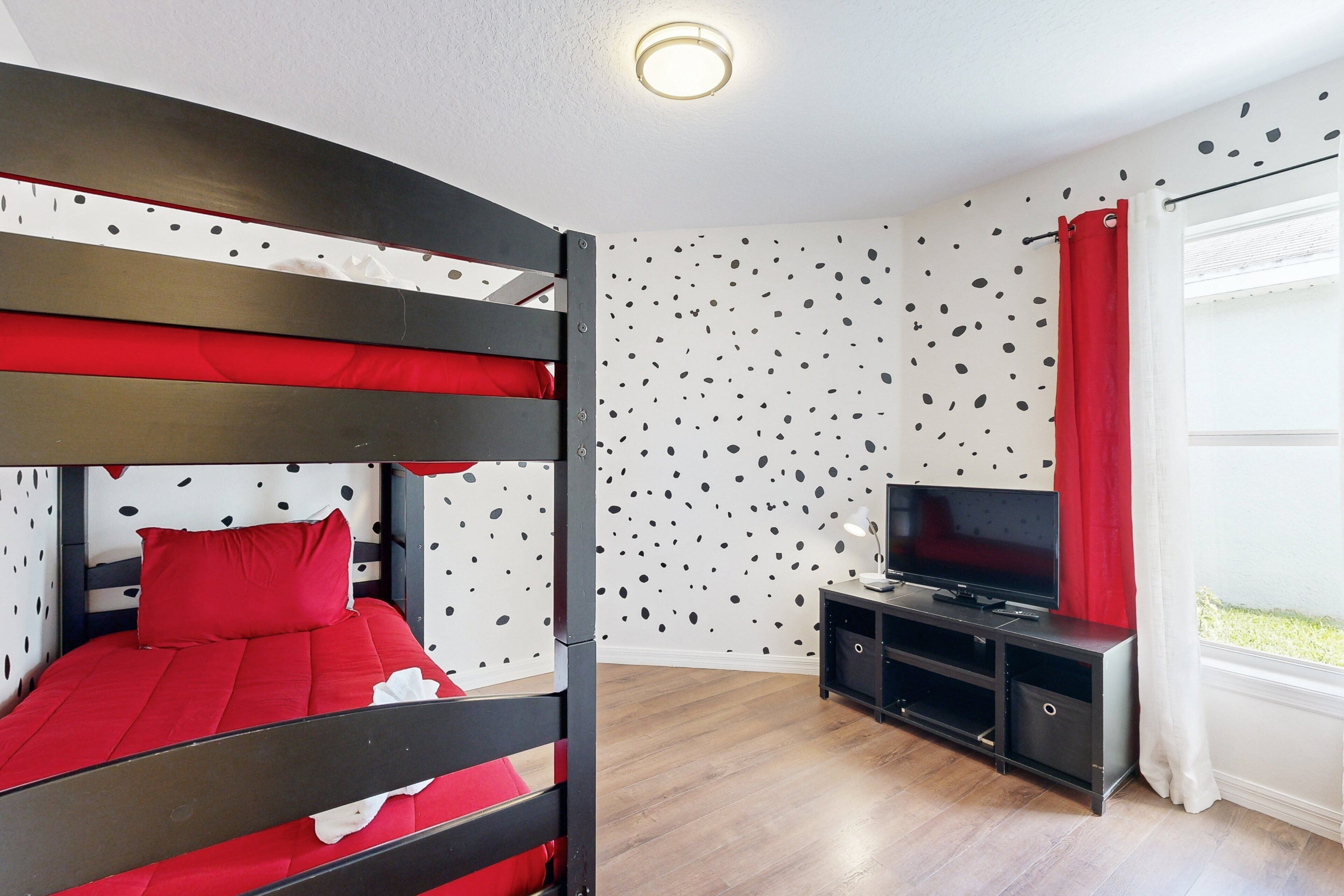 Una cama litera con ropa de cama roja, un televisor sobre un soporte negro y una pared con un diseño moteado.