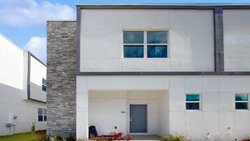 A modern two-story building with a stone accent wall, a blue door, and a small front garden.