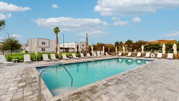 A swimming pool with lounge chairs, a paved deck, and a clear sky.