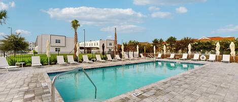 A swimming pool with lounge chairs, a paved deck, and a clear sky.