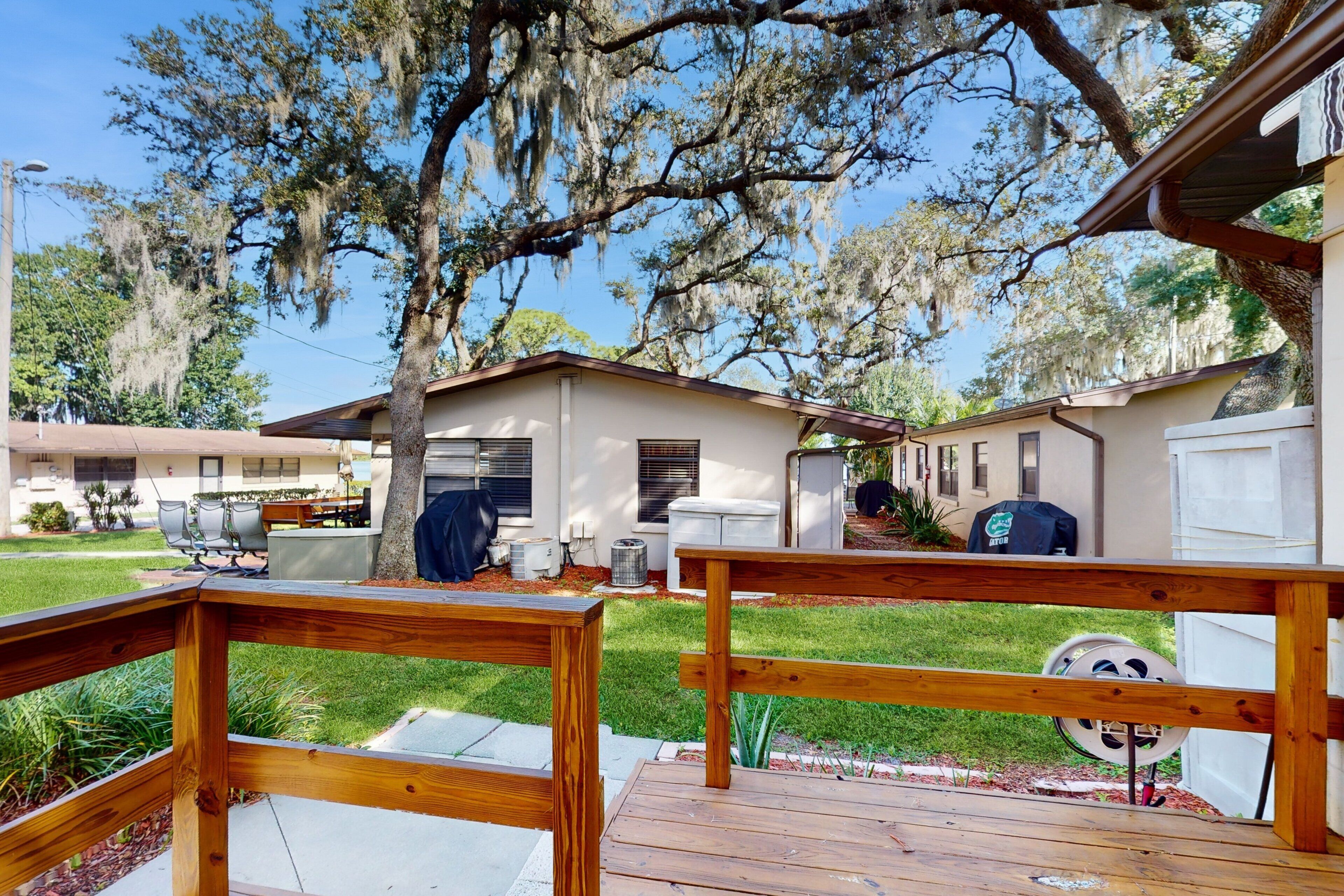 A wooden deck with a view of a residential area, including a house with a covered patio and a barbecue grill.