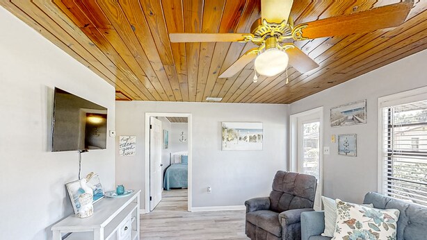 Uma sala de estar espaçosa com teto de madeira, um sofá cinzento, um console branco e um ventilador de teto.