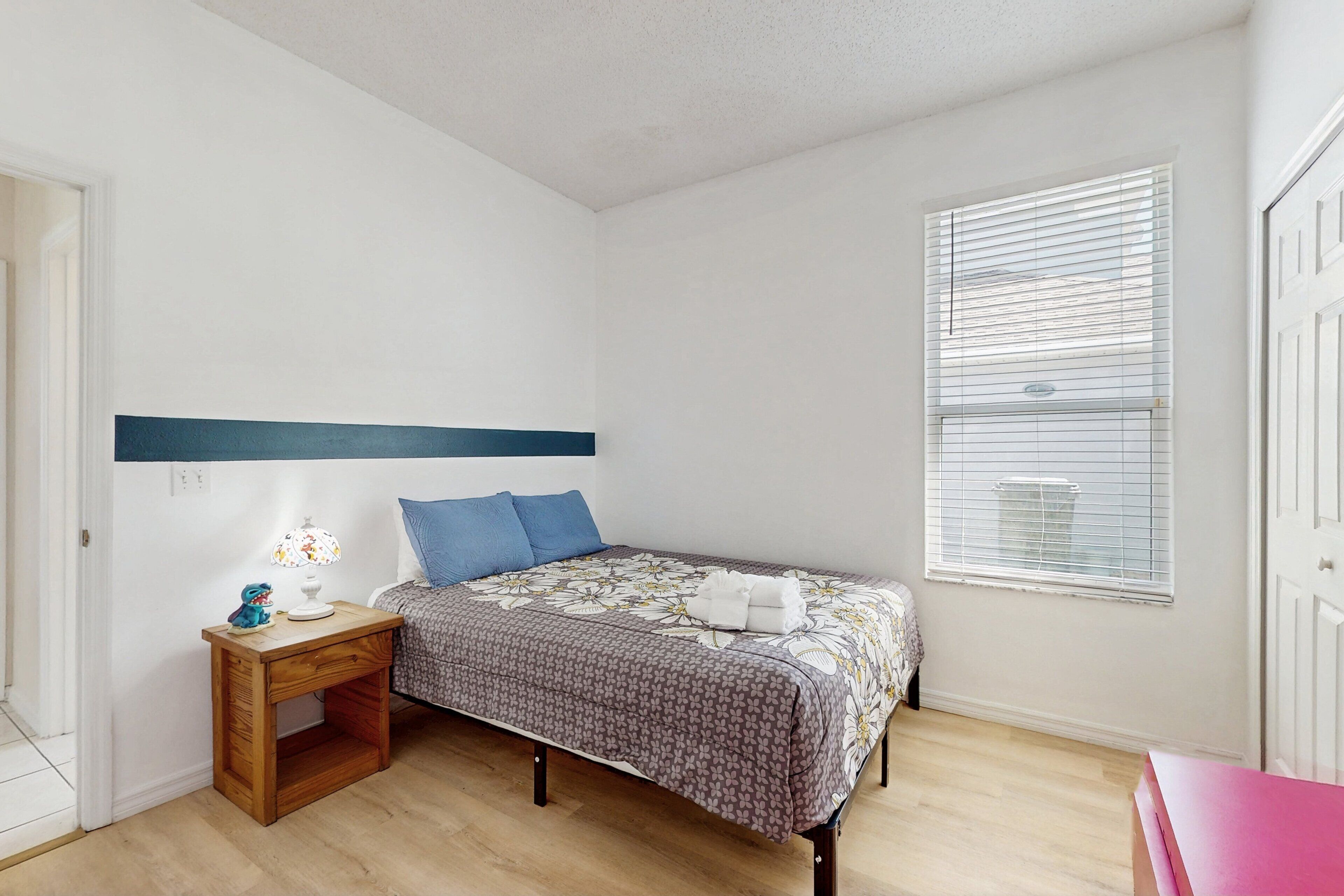 A bedroom with a bed, a nightstand, a lamp, and a window with blinds.