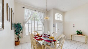 Un coin repas avec une table en verre, des chaises blanches, un lustre et une plante en pot.
