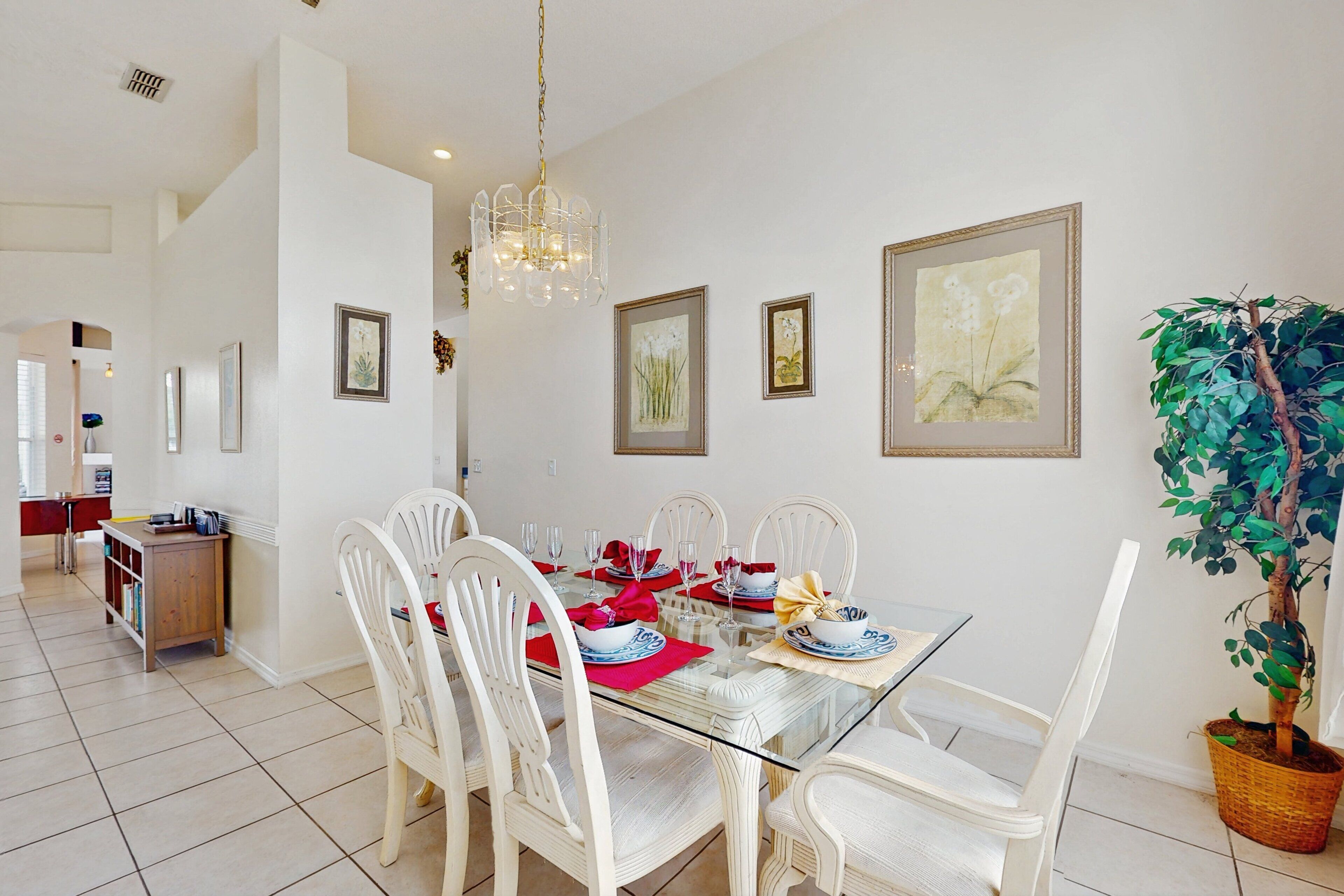 A dining area with a glass table, white chairs, and framed artwork on the walls.
