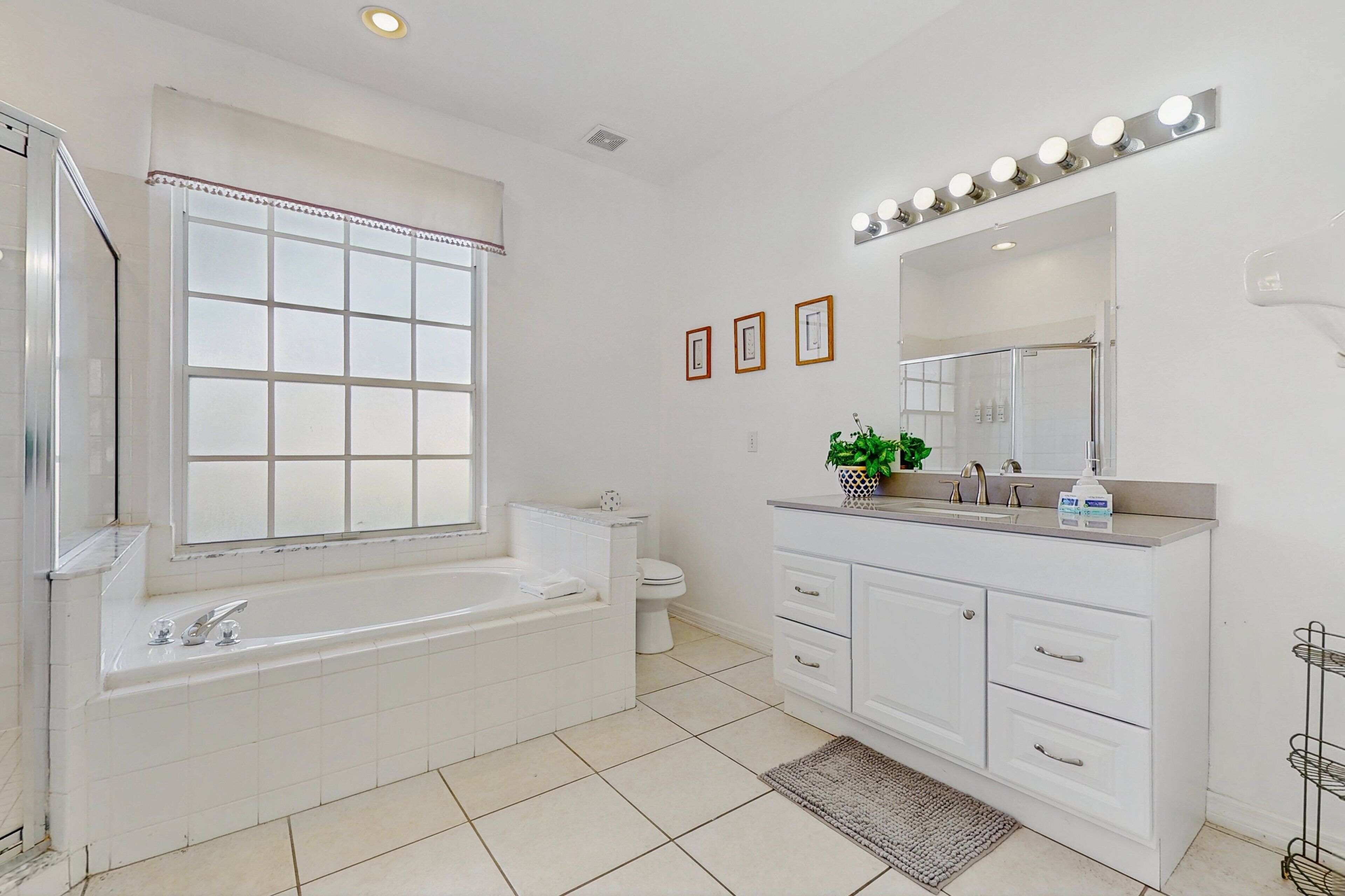Un baño moderno con bañera, inodoro, tocador y un espejo grande con luces.
