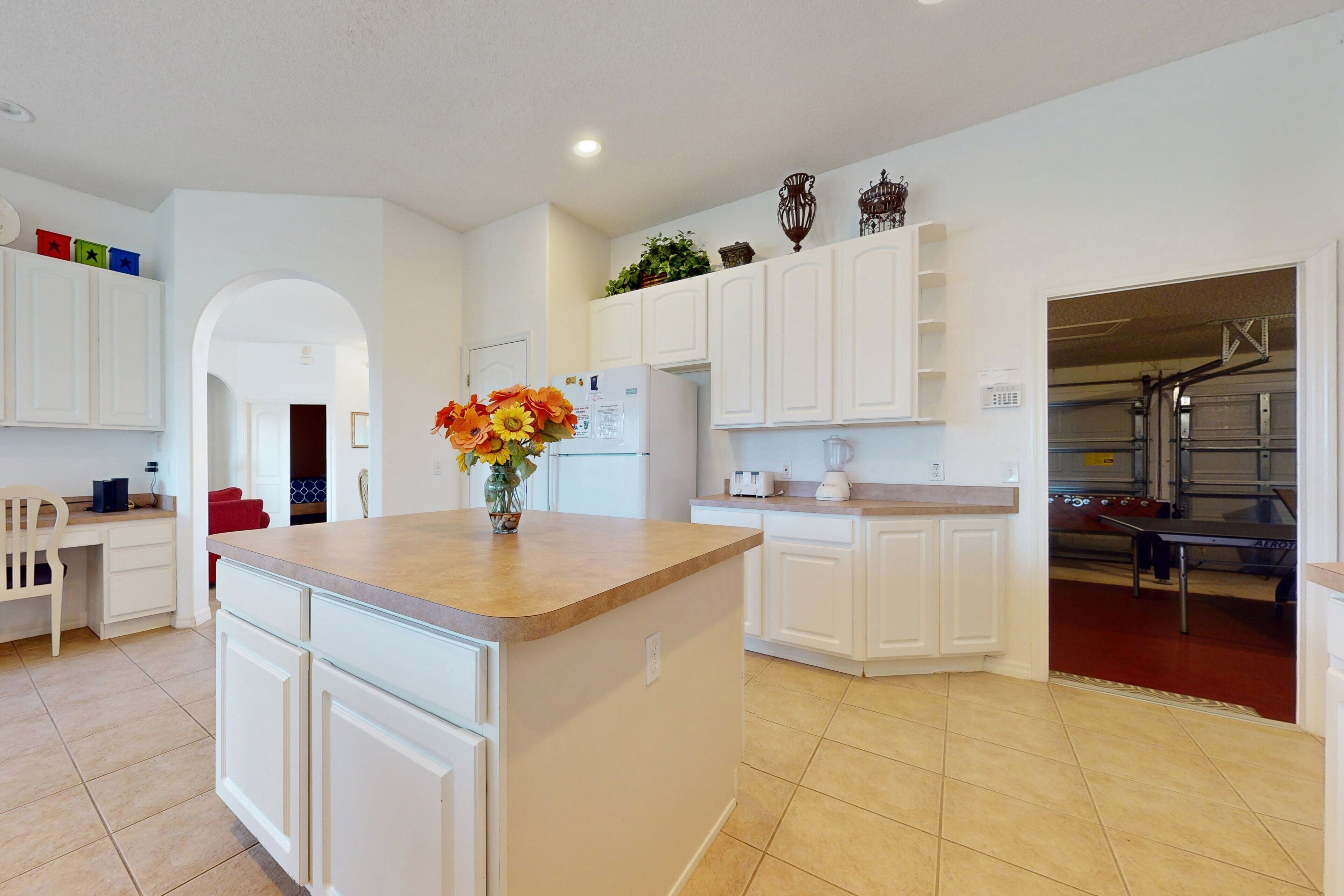 A modern kitchen with white cabinetry, a central island, and a dining area with a red chair.