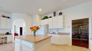 A modern kitchen with white cabinetry, a central island, and a dining area with a red chair. - Gated Community Home With Private Pool, Screened Lanai, & W/D - Near Disney/golf (Davenport)