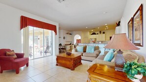A spacious living room with a red armchair, a wooden coffee table, a beige sofa with blue cushions, and a kitchen in the background. - Gated Community Home With Private Pool, Screened Lanai, & W/D - Near Disney/golf (Davenport)