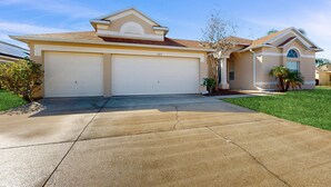A two-story house with a garage, a driveway, and a well-maintained lawn. - Gated Community Home With Private Pool, Screened Lanai, & W/D - Near Disney/golf (Davenport)