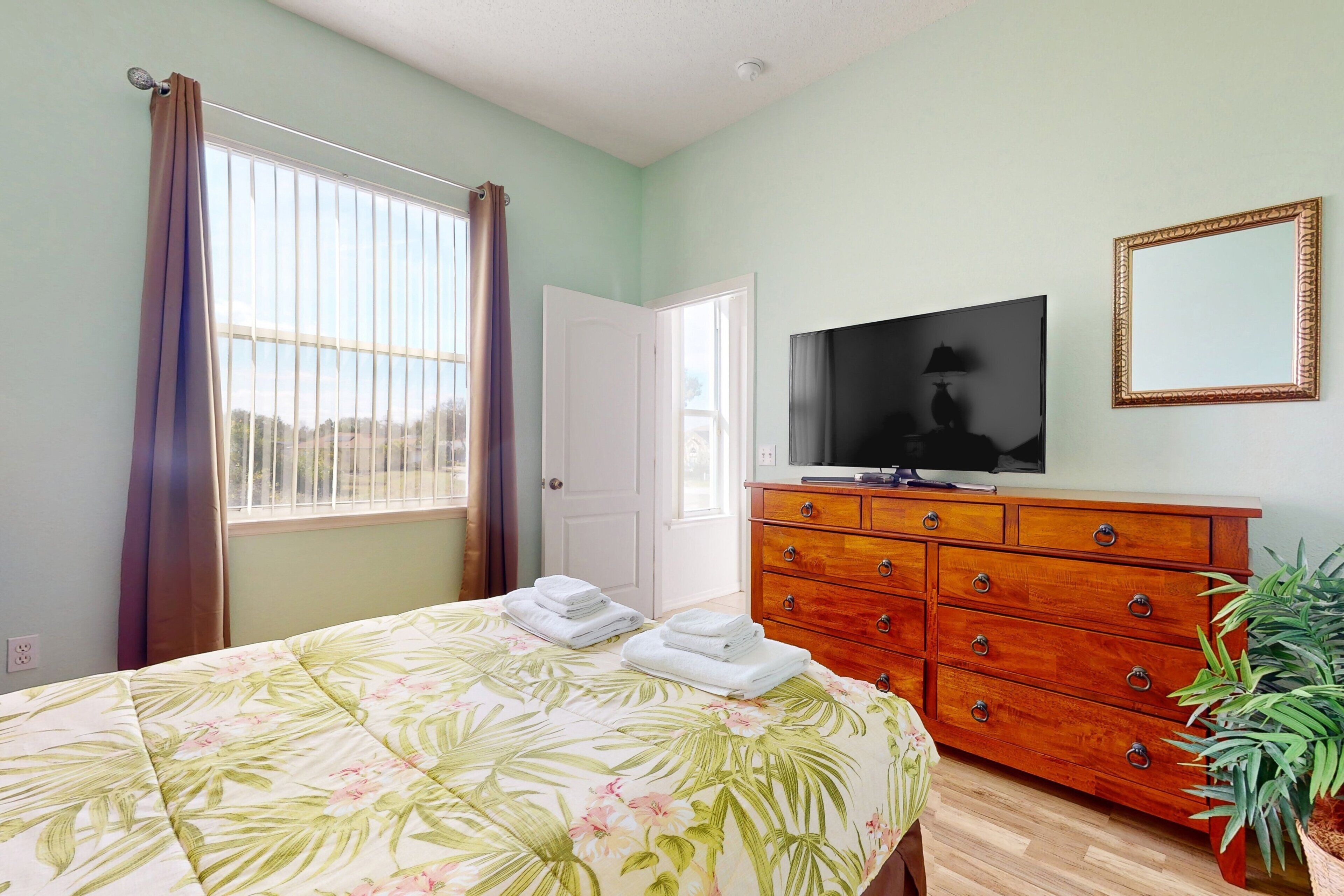 A bedroom with a bed, a TV, a dresser, and a plant.