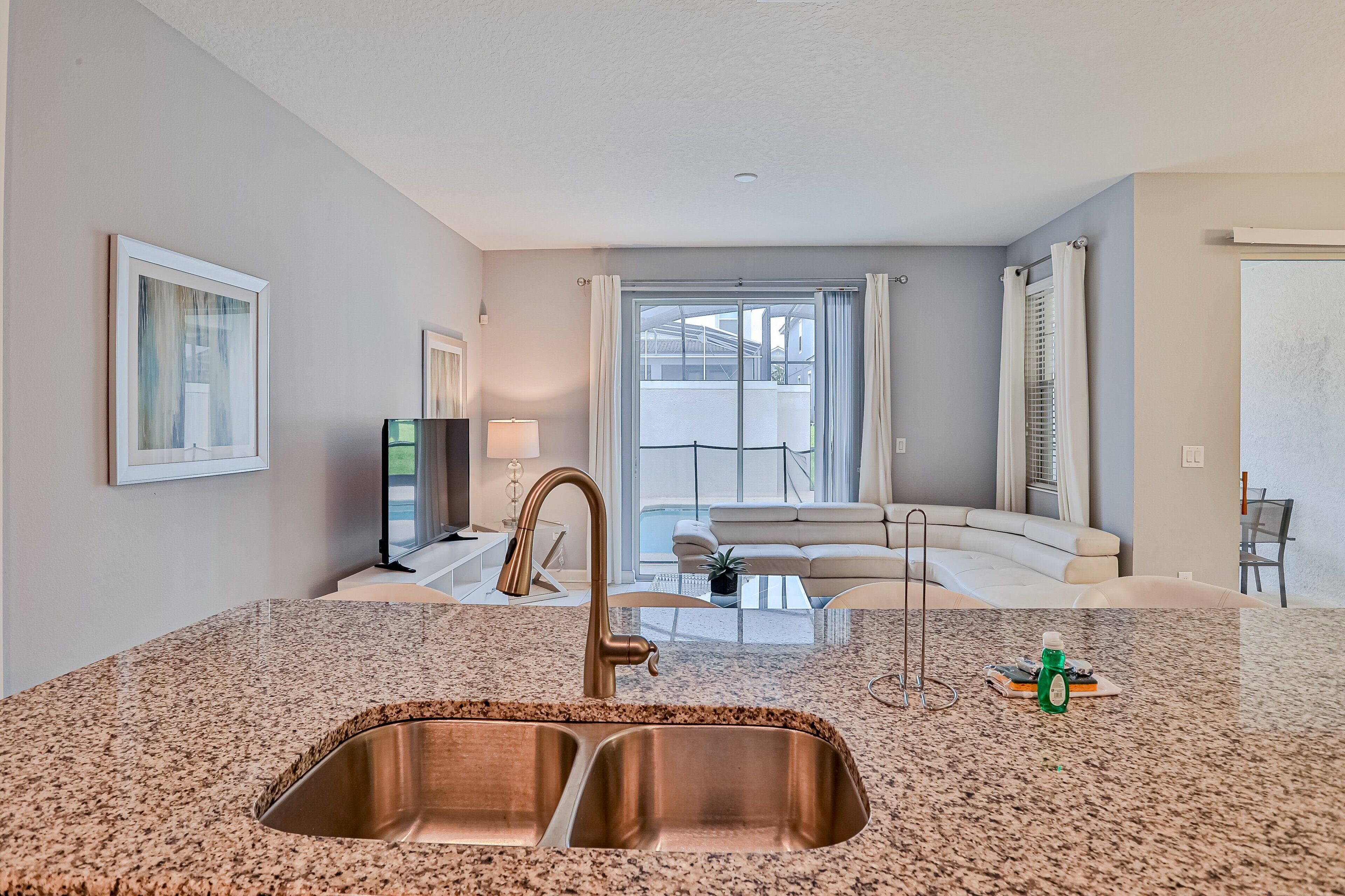 A modern kitchen with a granite countertop, stainless steel sink, and a dining area with a white table and chairs.