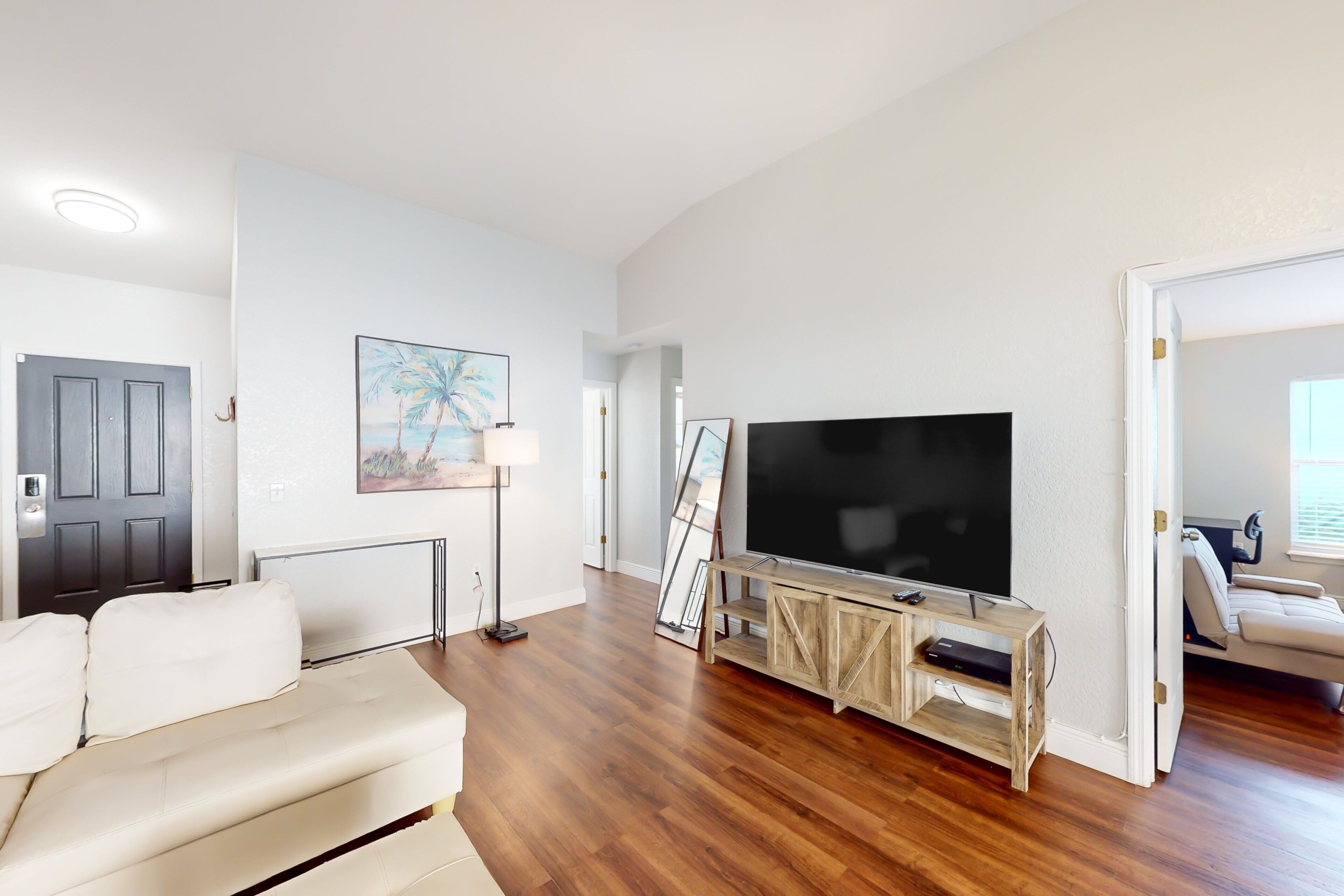 A living room with a large flat-screen TV, a sofa, a coffee table, and a painting on the wall.