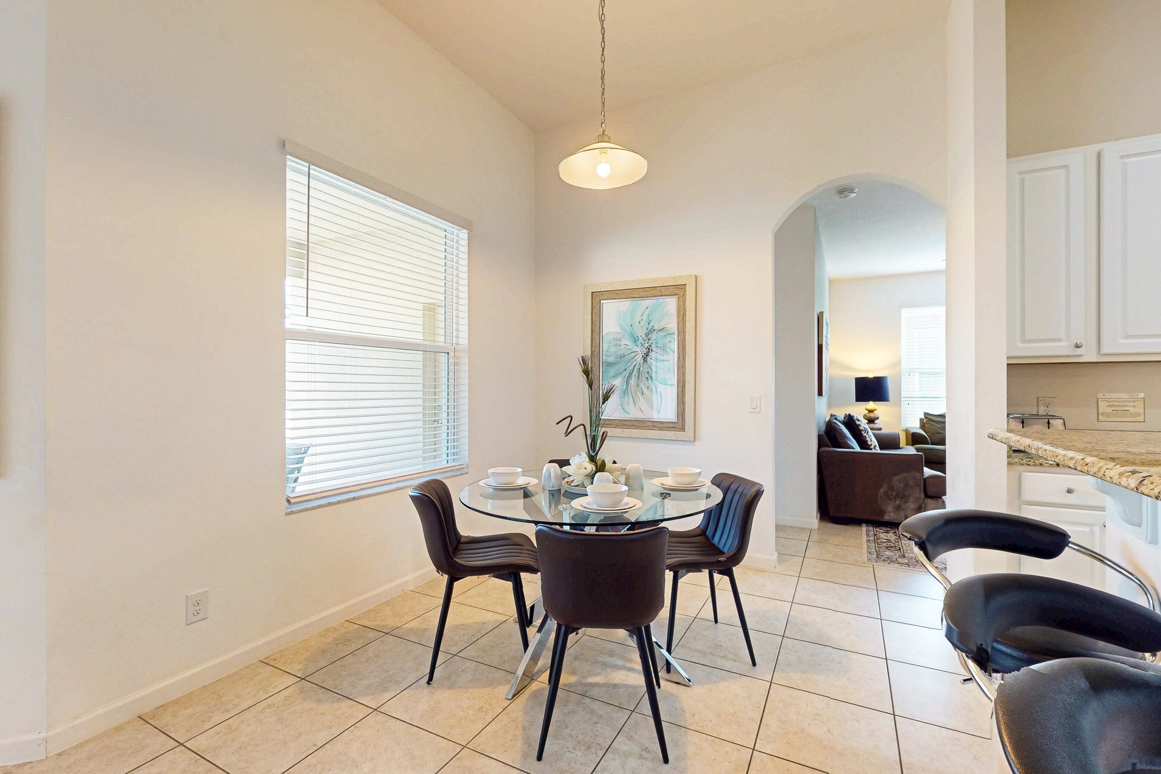 A dining area with a round glass table, four chairs, and a vase with flowers.