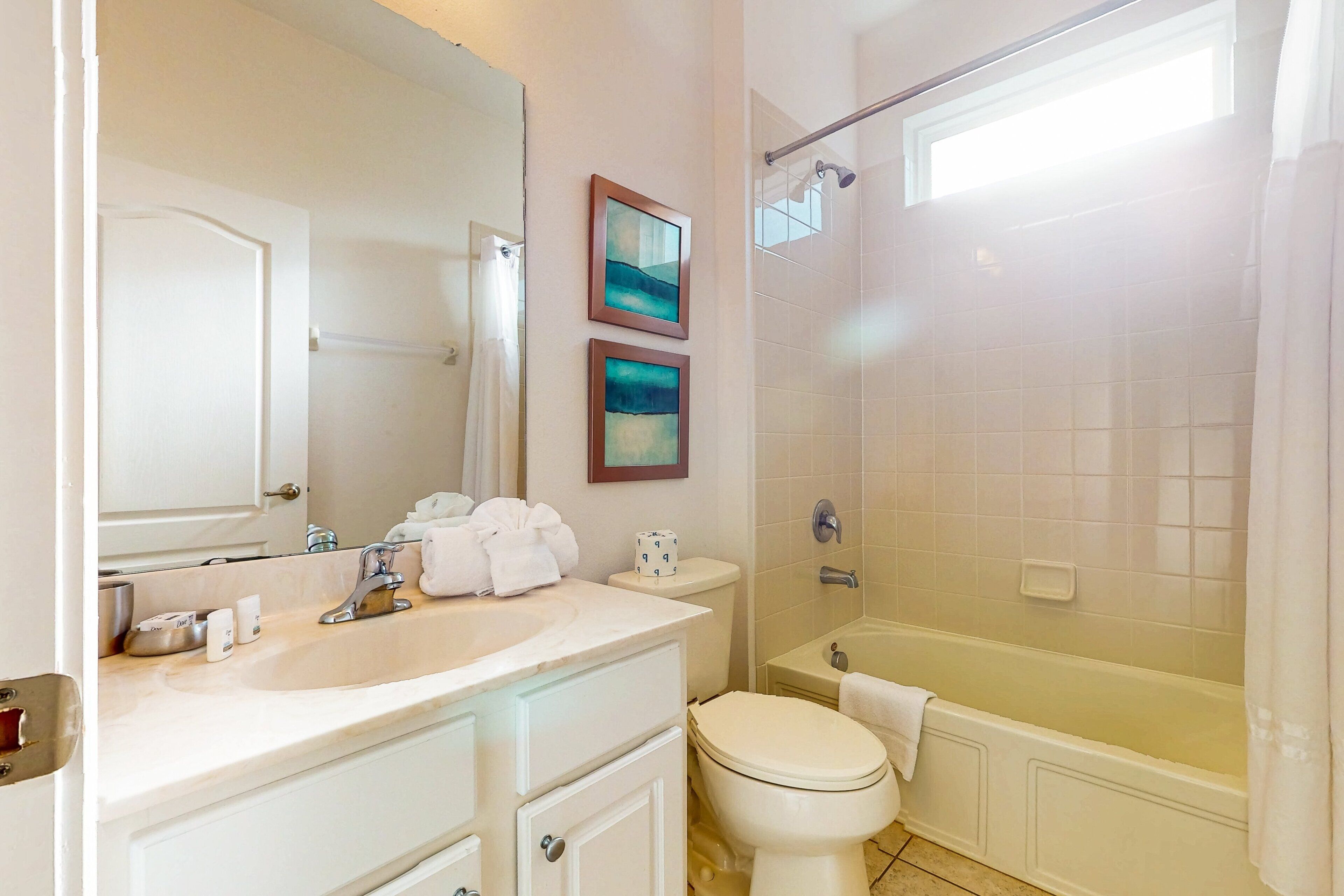 A bathroom with a white sink, toilet, and bathtub, with a window and a shower curtain.