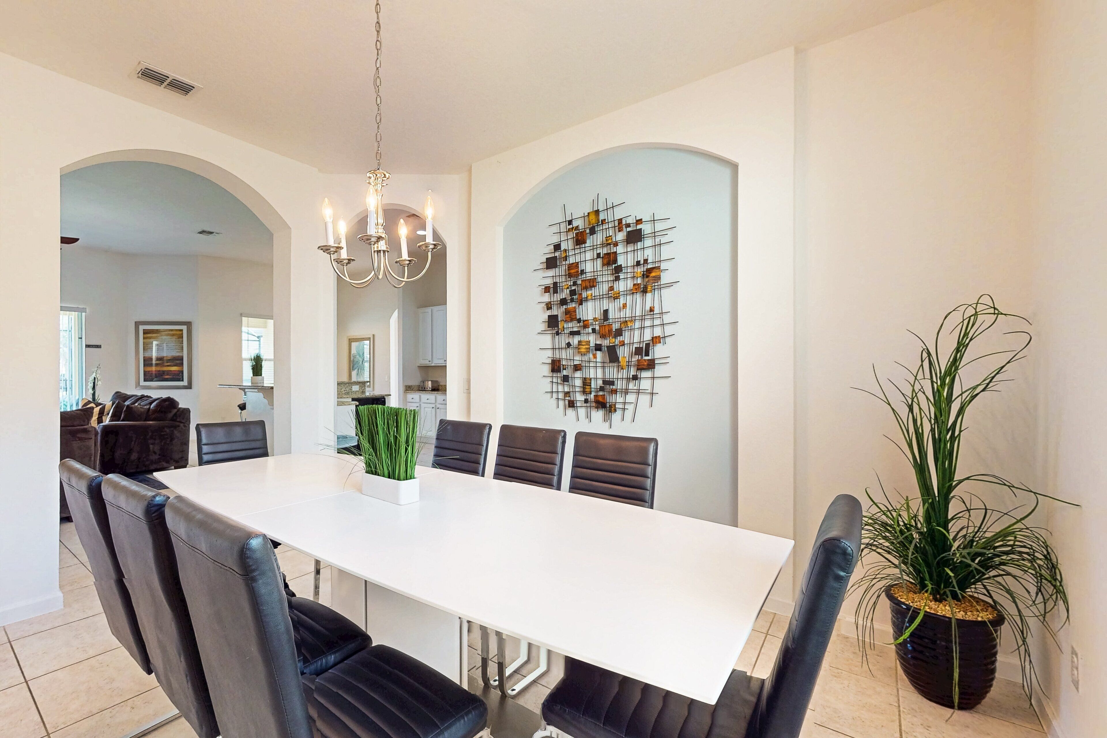 Un coin repas avec une table blanche, des chaises noires, un lustre et un élément décoratif mural.