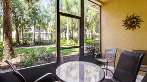 A room with a glass table and chairs, large windows with a view of trees and a building, and a decorative wall piece. - Bright, Centrally-located Getaway With a Pool, Clubhouse, & Fast Wifi (Kissimmee)