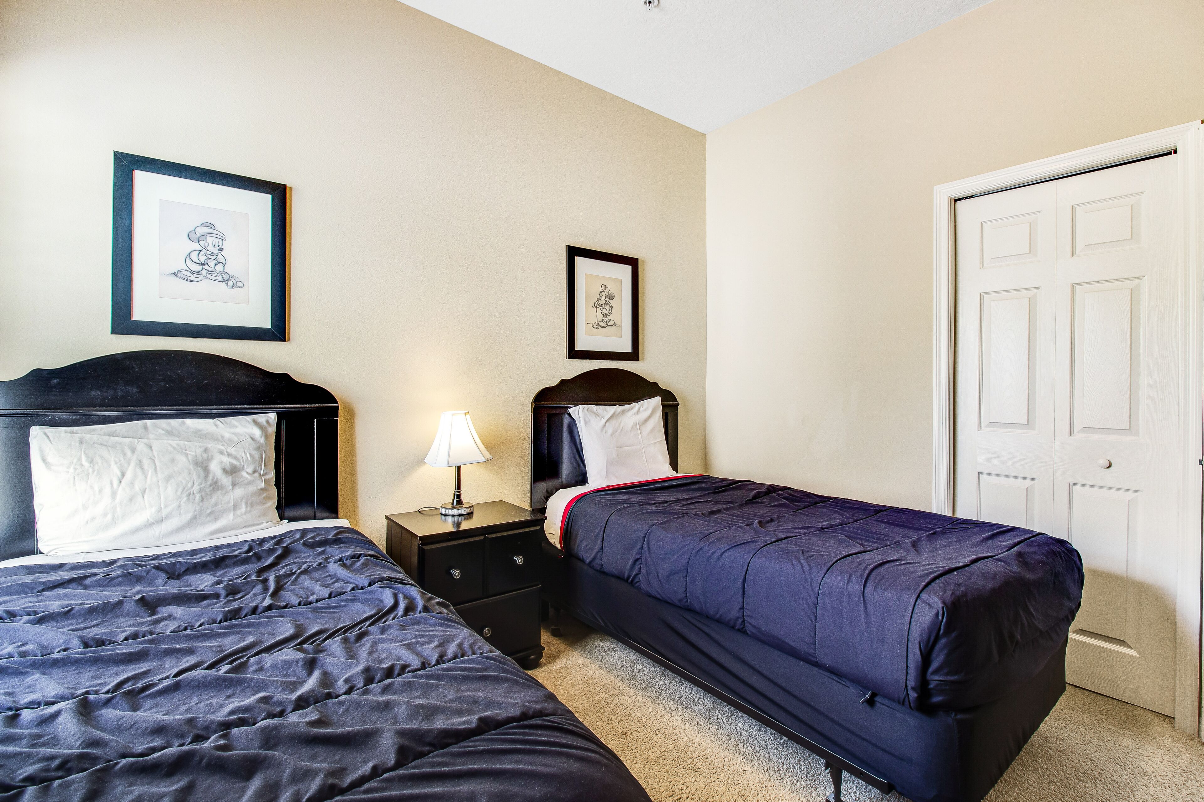 A bedroom with two beds, a nightstand with a lamp, and two framed pictures on the wall.