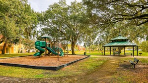 Un'area giochi con scivolo e struttura per arrampicarsi, circondata da alberi e un gazebo.