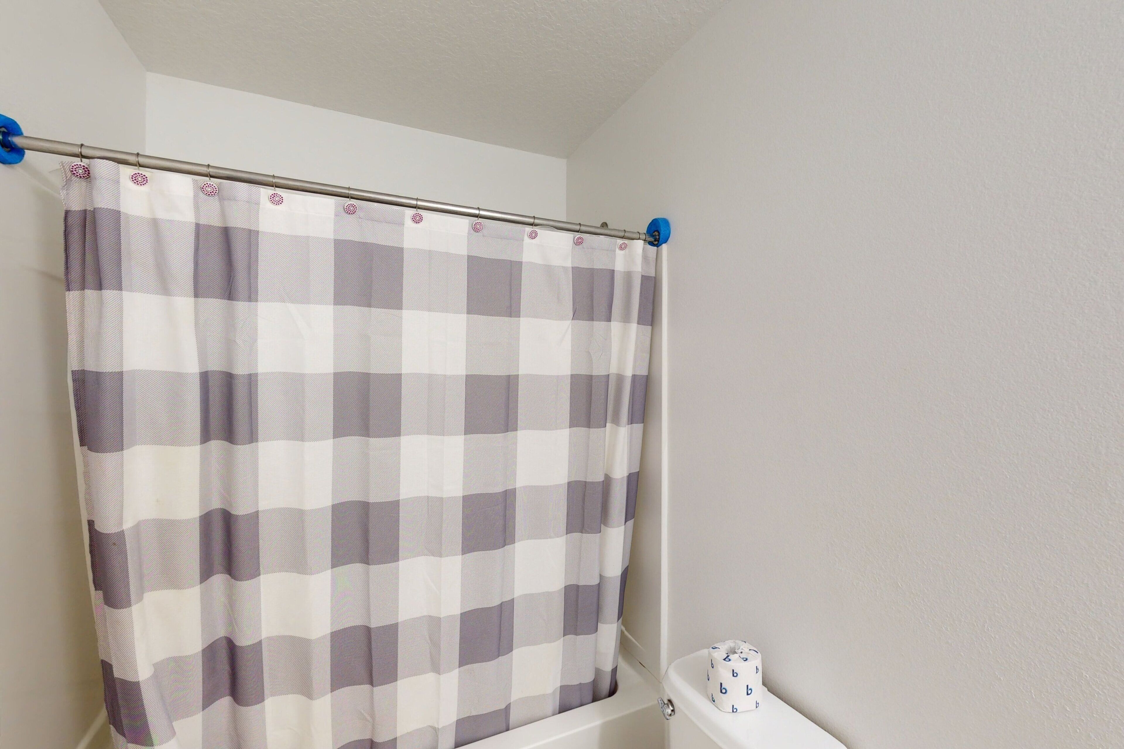 A bathroom with a checkered shower curtain, a white bathtub, and a toilet with a blue and white design.