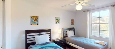 A bedroom with two beds, a ceiling fan, and posters on the walls.