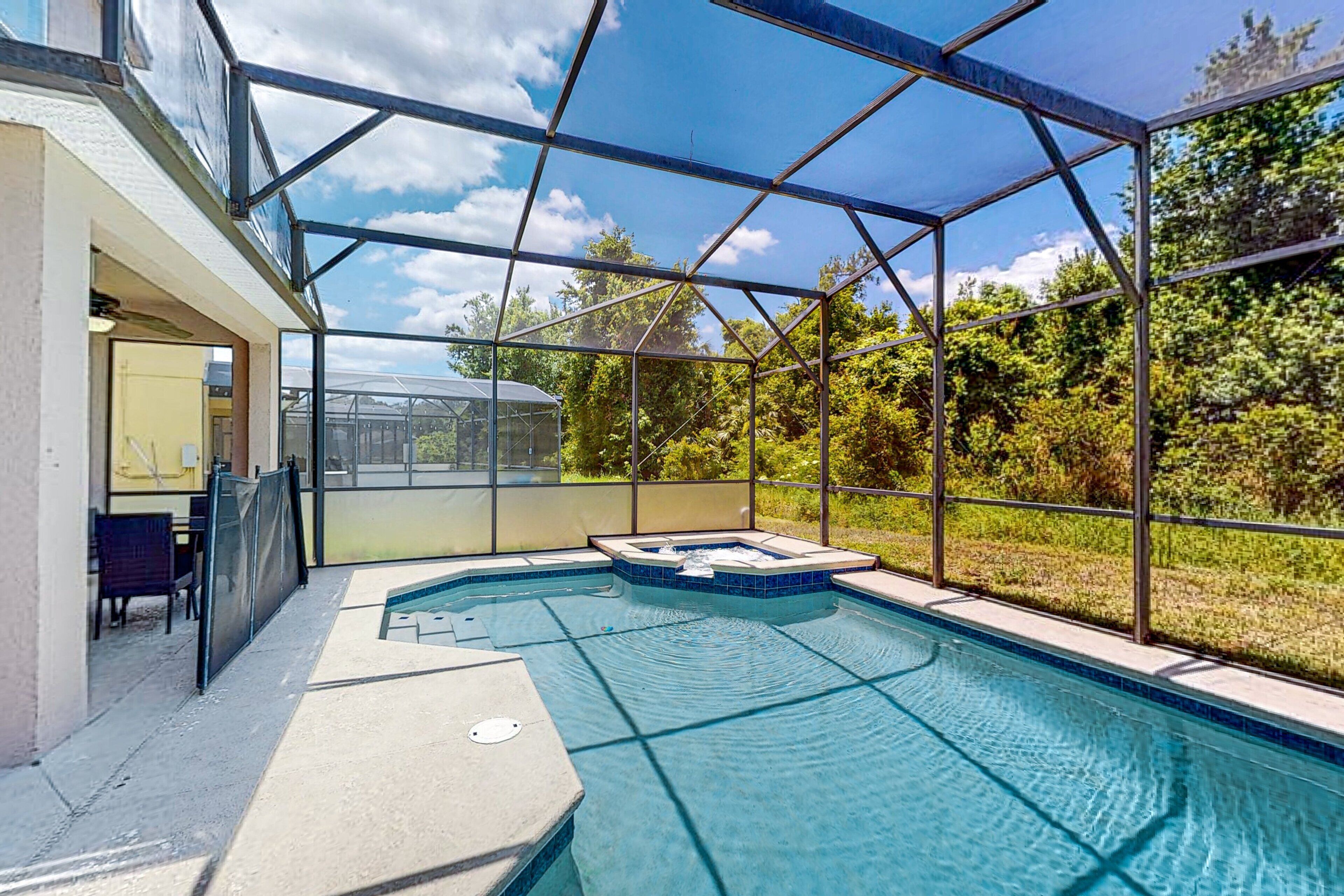 A swimming pool with a glass enclosure, a hot tub, and a view of the surrounding greenery.