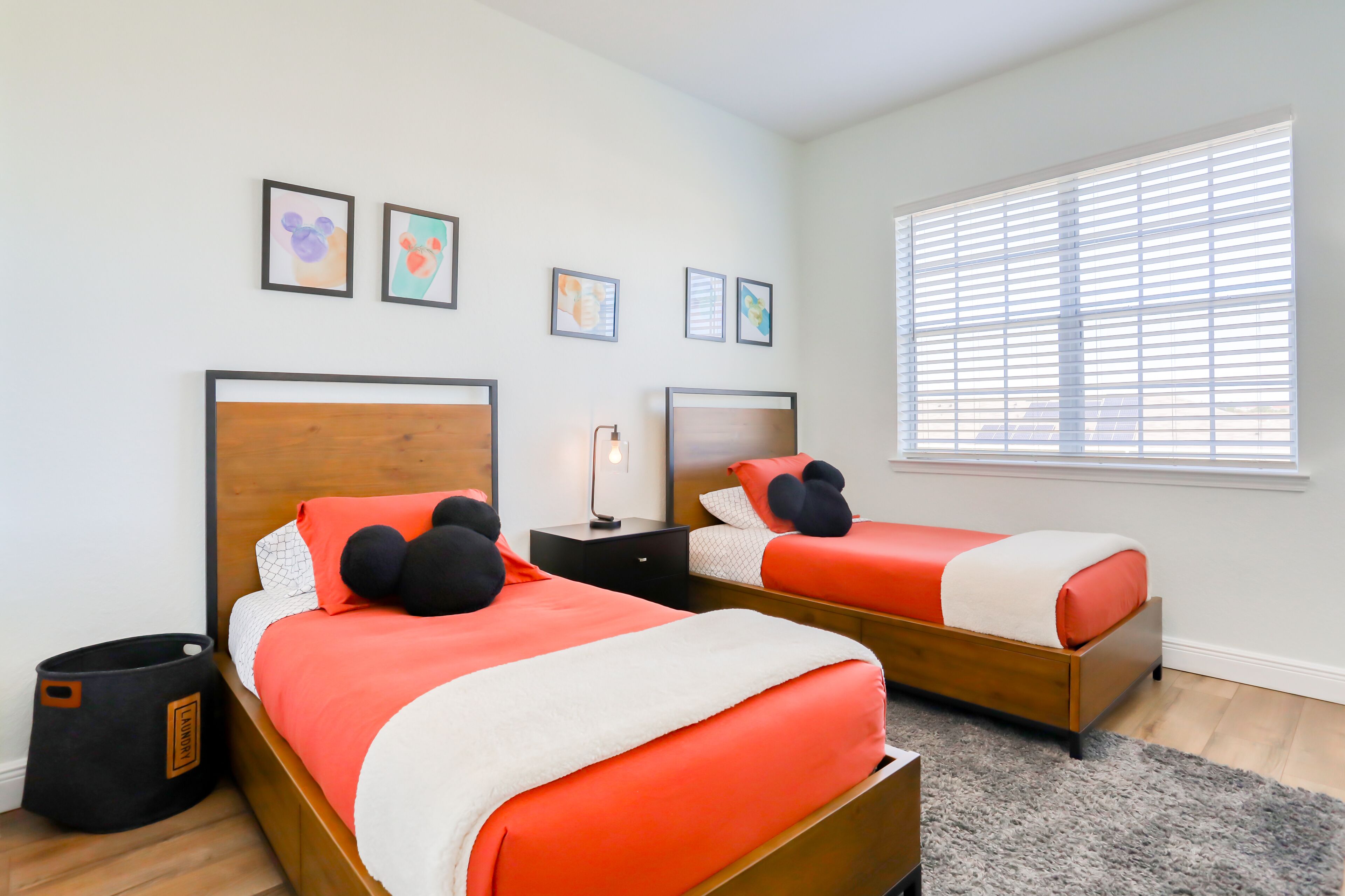 A bedroom with two beds, a nightstand, a trash can, and a window with blinds.