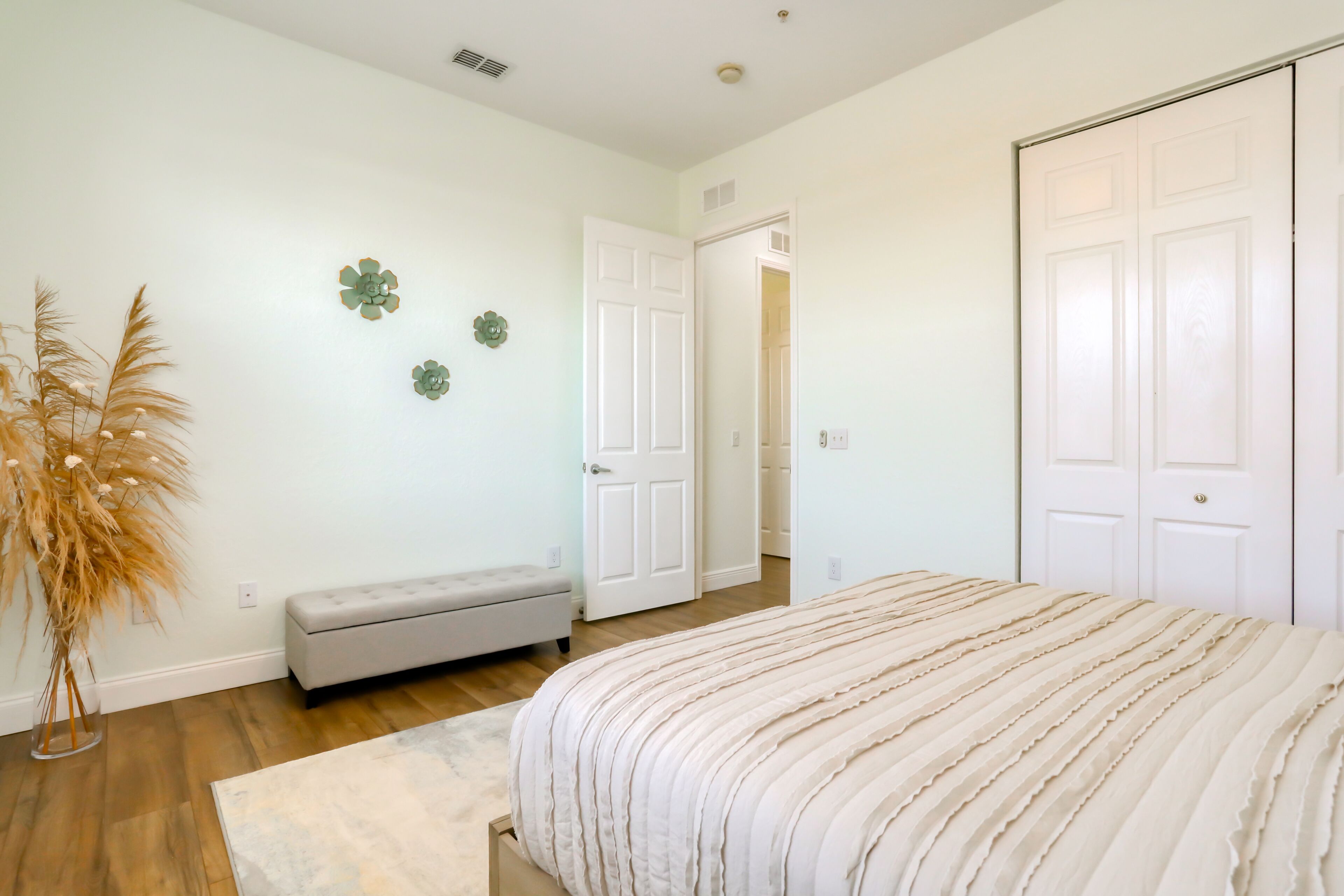 A bedroom with a bed, a bench, and a door leading to another room.