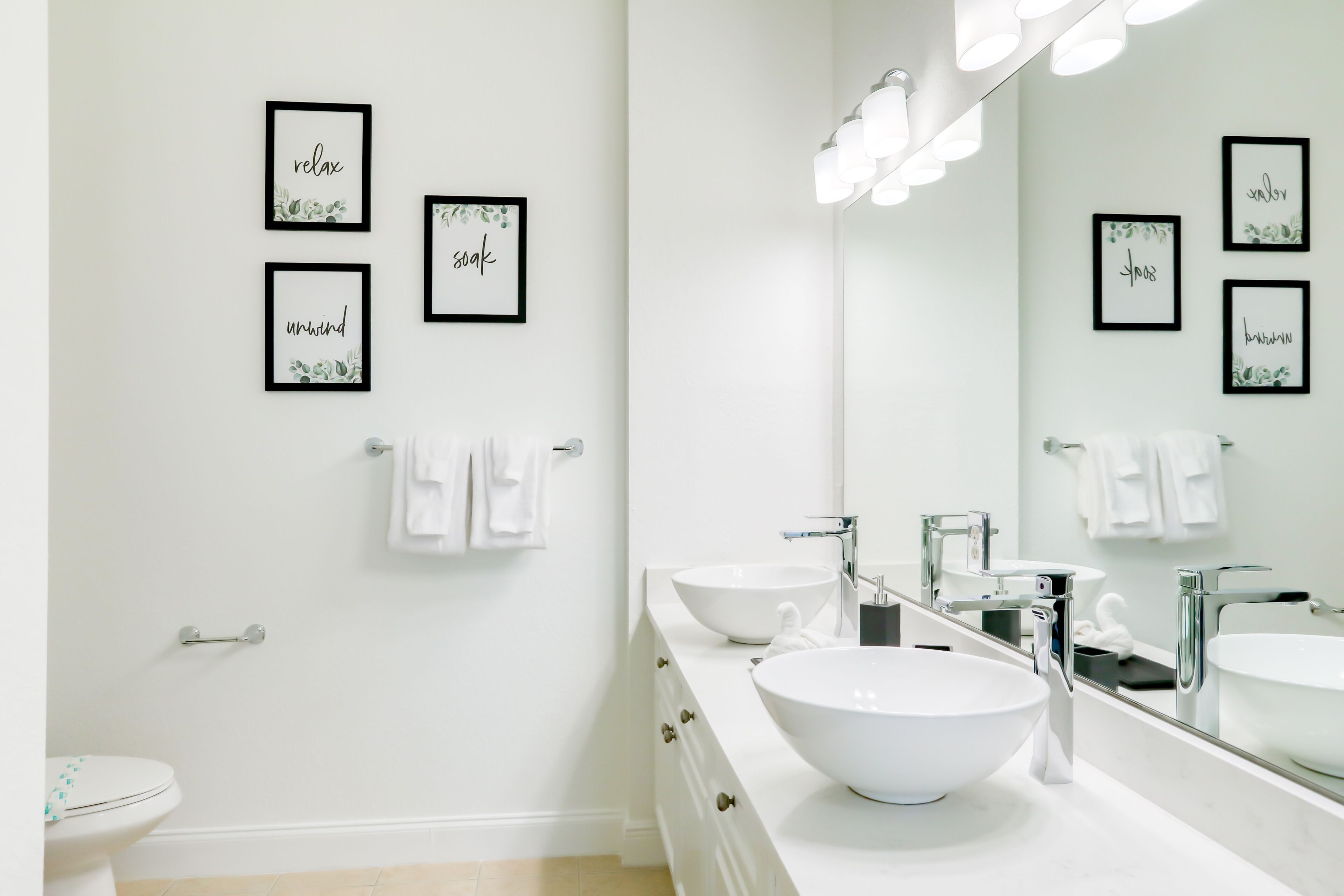 A modern bathroom with two sinks, a large mirror, and framed motivational quotes on the wall.