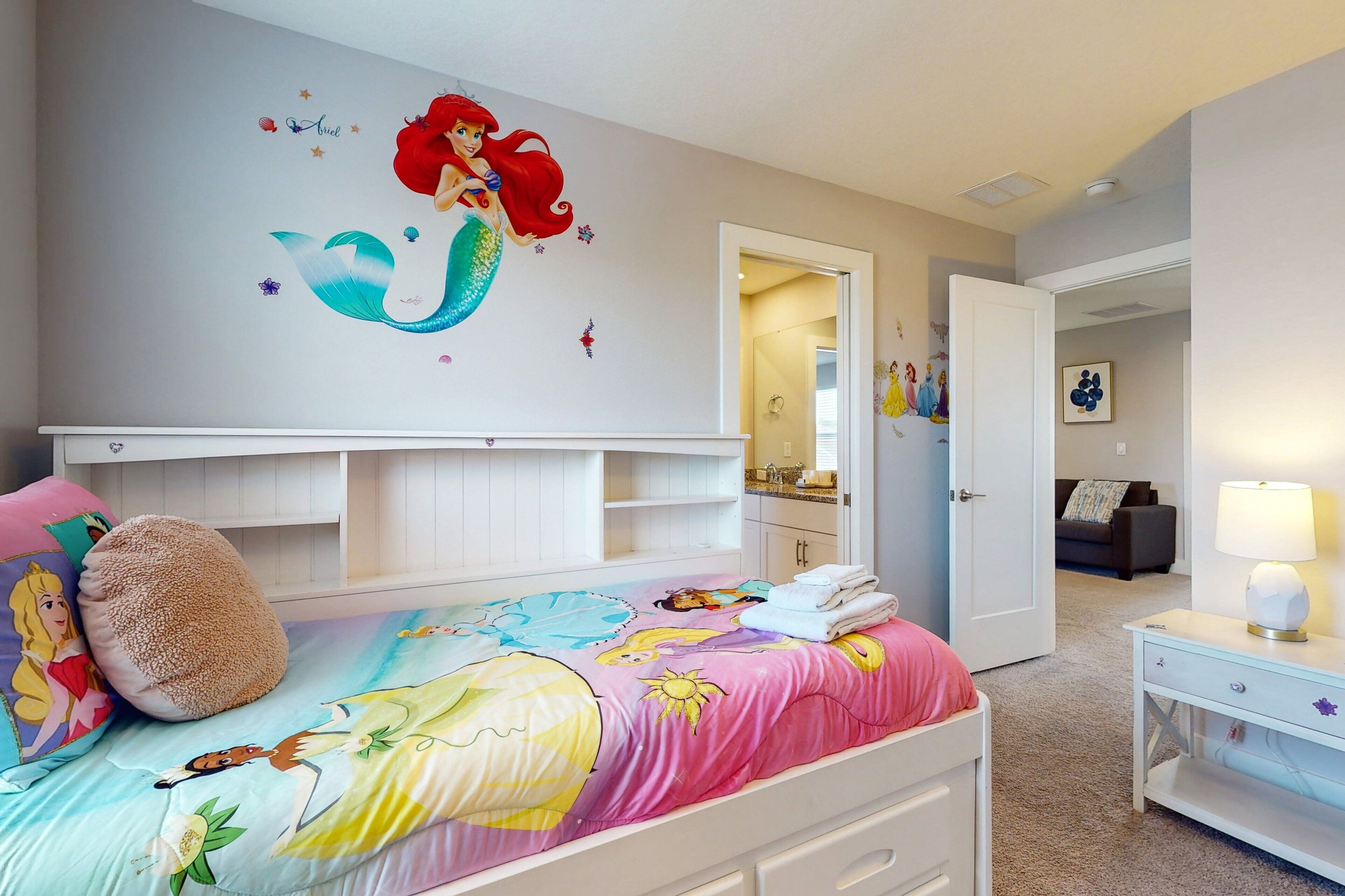 Quarto de criança com cama, cômoda, mesa de cabeceira e porta que dá para outro espaço.