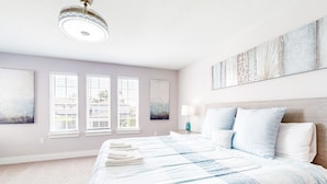 A bedroom with a large bed, a nightstand with a lamp, and artwork on the walls. - Bright Home With Private Pool, Washer/dryer and Internet (Kissimmee)