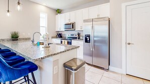 A modern kitchen with white cabinets, stainless steel appliances, a granite countertop, and blue bar stools. - Bright Home With Private Pool, Washer/dryer and Internet (Kissimmee)