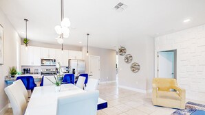 A modern kitchen with white cabinets, a dining area with a white table and blue chairs, and a yellow armchair in a living room with a patterned rug. - Bright Home With Private Pool, Washer/dryer and Internet (Kissimmee)