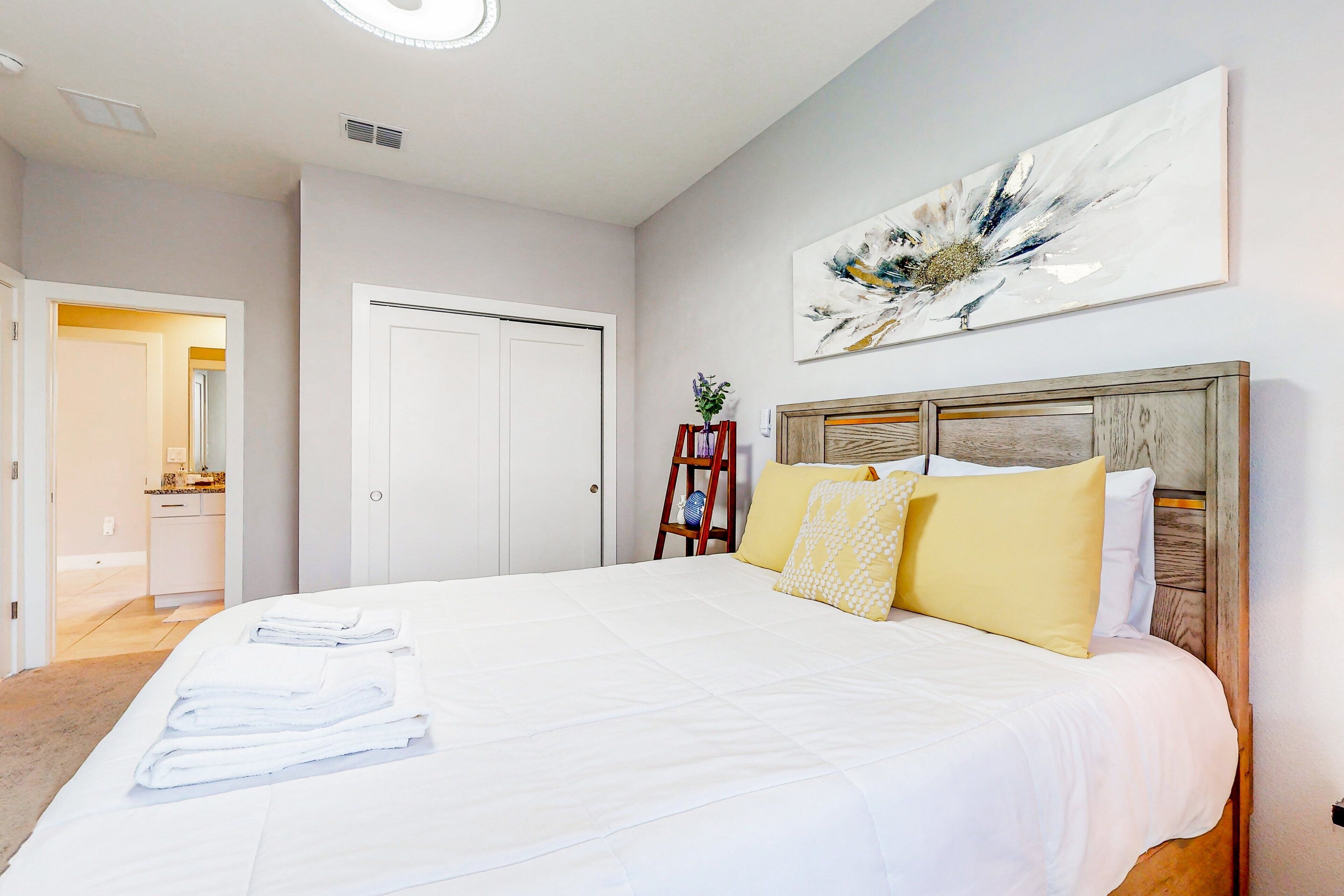A hotel room with a large bed, a wooden headboard, a painting on the wall, and a door leading to a bathroom.
